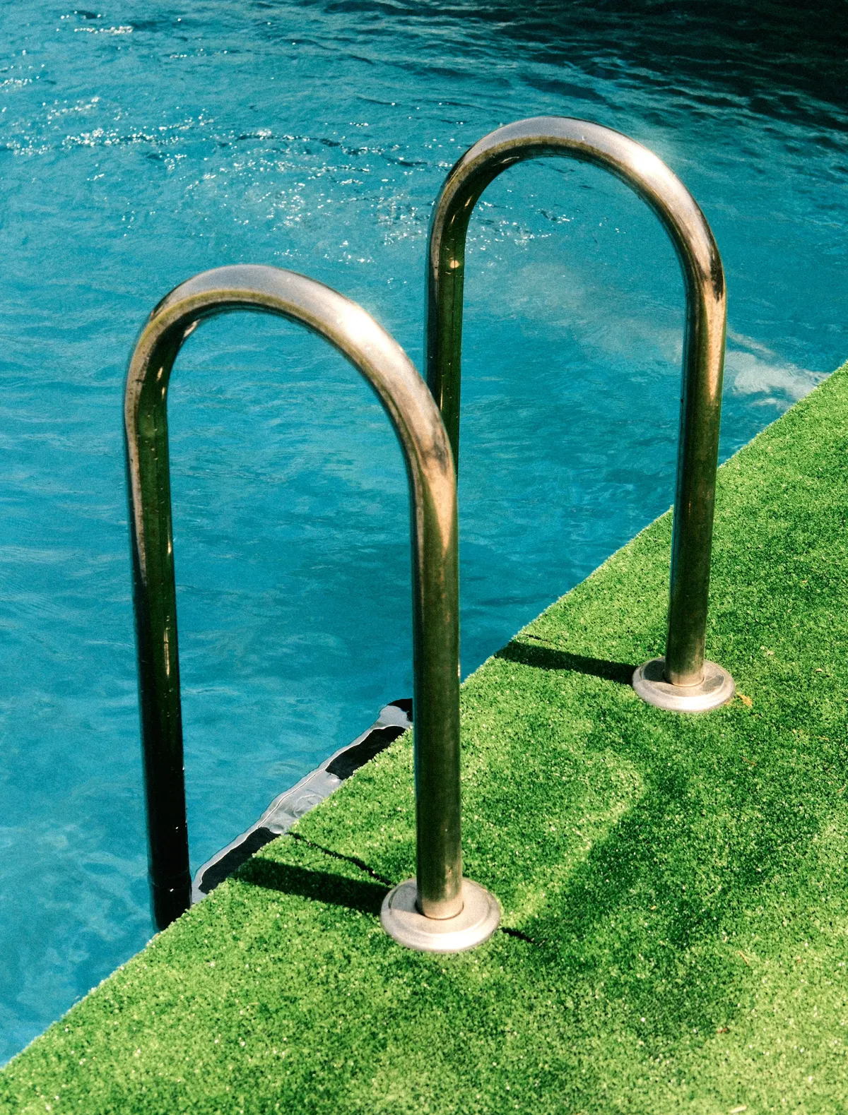 Artificial grass at the edge of a backyard pool with a steel ladder